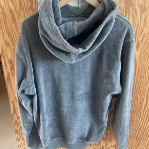 Grå hoodie - Säljer en stilren grå hoodie med en stor ficka framtill och justerbar huva. Perfekt för en avslappnad look. 