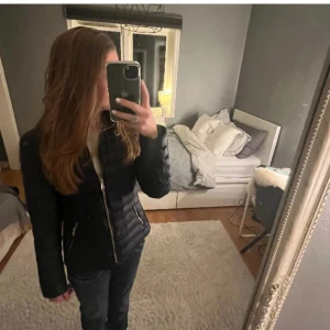 Svart dunjacka med dragkedja - Snygg svart dunjacka med dragkedja framtill. Jackan har en figurnära passform och är perfekt för kyligare dagar. Den har långa ärmar och en stilren design som passar till det mesta.