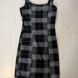 Svart och grå rutig klänning från H&M Divided - Snygg svart och grå rutig klänning från H&M Divided. Klänningen har en figurnära passform med en dragkedja på sidan för enkel påklädning. Perfekt för en stilren look eller för att lagra!
