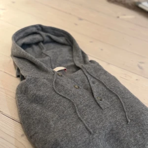 Grå hoodie med knappar - Säljer en stilren grå hoodie med knappar framtill och justerbar huva. Perfekt för en avslappnad look. Den är långärmad och gjord i ett mjukt material som känns skönt mot huden.