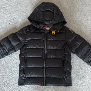 Svart dunjacka från Parajumpers - Säljer en snygg svart dunjacka från Parajumpers med huva och dragkedja. Använd 1 vinter, bra skick. Du får med lapparna som satt på dragkedjan. Jackan är i storlek junior medium men skulle säga att den passar folk runt 163-170