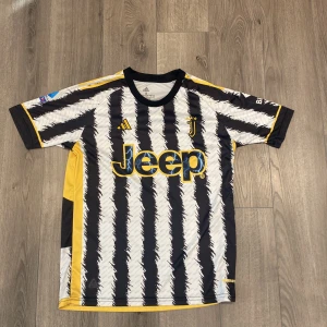 Juventus matchtröja - Juventus fotbollströja från Adidas med svartvita zebraränder och gula detaljer. Jeep-logga på bröstet, klubbmärke och Adidas-logga i gult. Kortärmad modell i lätt och ventilerande material, perfekt för fotbollsplanen eller att bära till vardags. Storlek S (passar också M )