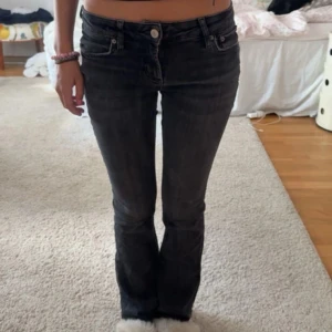 Svarta bootcut jeans från Zara - Snygga svarta jeans från Zara med bootcut passform och låg midja. Jeansen har klassiska fem fickor, bälteshällor och dragkedja med knapp. Materialet är stretchigt jeans som sitter tajt upptill och släpper ut vid anklarna. Perfekta till sneakers eller boots.