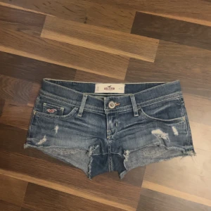 Blå jeansshorts från Hollister - Snygga blå jeansshorts från Hollister med låg midja och slitna detaljer. Klassisk femficksmodell med råa kanter och broderade bakfickor. Perfekt för dig som gillar en avslappnad och cool stil under varma dagar.