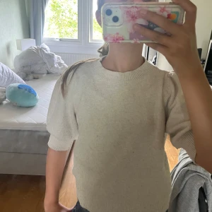 Beige stickad tröja från Vero Moda - Superfin beige stickad tröja från Vero Moda med puffiga ärmar och rund halsringning. Tröjan har kortare ärmar och är gjord i en mjuk polyesterblandning. Perfekt att styla med jeans eller kjol för en chill look.