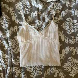 Vit ribbad linnetopp med spets H&M - Supersöt vit ribbad linnetopp från H&M Divided med smala axelband och spetsdetaljer längs v-ringningen. Strl S💓💓