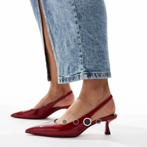 WIDE FIT Röda pumps med spetsig tå - Helt nya snygga röda pumps med Wide Fit med glansig finish och spetsig tå. Skorna har en öppen häl med smal rem och låg klack som ger en cool siluett. 