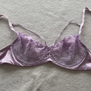 Ljuslila spetsig bh  - Superfin ljuslila bh med tunna axelband och vackra spetsdetaljer framtill. Den har blommigt spetsmönster och dekorativa band över bysten. Används framförallt som en bh men kan självklart stylas så som på bilden. 