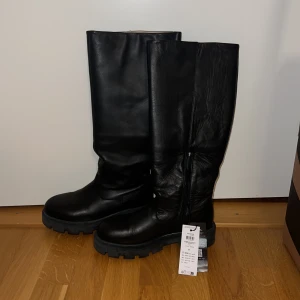 Svarta höga läderstövlar Selected - Aldrig använda. Snygga svarta stövlar i äkta skinn från Selected Femme. Modellen är högskaftad med grov sula och dragkedja på insidan. Perfekta för att lyfta din outfit med en cool och stilren look. Nypris: 2400kr.