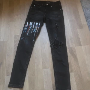 Amiri Jeans - Svarta jeans från Amiri med skinny fit, coola slitningar och färgstänk i blått, rött, vitt och orange på ena benet. Stort AMIRI-tryck framtill. Klassisk femficksmodell och knappgylf. Perfekta för dig som vill sticka ut. Kom med bud 