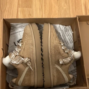 Beige sneakers från UGG med fårfoder - Chunky sneakers från UGG i beige mocka och textil med breda, mönstrade snören och fluffigt vitt fårfoder. Grov sula och rund tå ger en cool look, perfekt för kalla dagar. UGG-logga på sidan och hälflik för enkel påtagning. Använda 1 gång och kommer ej till användning mer. Pris kan diskuteras