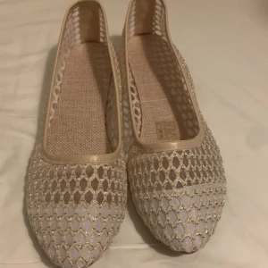 Beige ballerinaskor med nät och glitter - Snygga ballerinaskor i beige med glittrigt nätmönster och rund tå. Skorna har platt sula och är tillverkade i syntetmaterial med transparenta detaljer. Perfekta för dig som gillar en luftig och lätt stil.