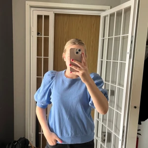 Blå puffärmströja från Lindex - Supersöt ljusblå tröja från Lindex med puffiga ärmar och rund halsringning. Tröjan har en loose passform och är gjord i mjuk bomull, perfekt för dig som gillar en chill men ändå trendig stil. Passar lika bra till jeans som kjol.