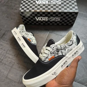 Svarta och vita Vans x SNS sneakers - Unika Vans x SNS sneakers i svart och vitt med grafiskt mönster på ovandelen och SNS-logga på sulan. Skorna har klassisk låg profil, vita snören och orange Vans-detalj. Perfekta för dig som gillar streetstyle och vill sticka ut.