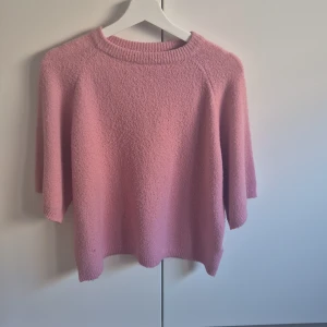 Rosa stickad tröja med trekvartsärm - Säljer en supermysig rosa stickad tröja med trekvartsärm och rund hals. Tröjan har en loose passform och är perfekt för dig som gillar en chill och avslappnad stil. Materialet är mjukt och fluffigt, vilket gör den extra skön att ha på sig.