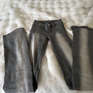 Grå jeans från Cheap Monday - Säljer ett par grå jeans från Cheap Monday med snyggt slitna detaljer och raka ben. Jeansen har klassiska fem fickor, bälteshällor och en grön etikett bak. Materialet är jeans och passformen är normal med straight stil.