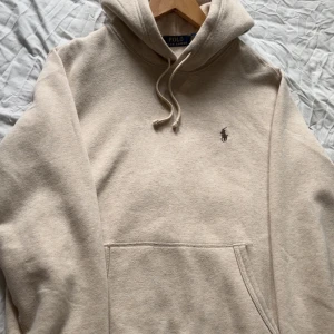 Beige hoodie från Polo Ralph Lauren - Tja, Säljer en aldrig avvänd beige hoodie från Polo Ralph Lauren i storlek M(passar även S). Tröjan har huva med snörning, klassisk känguruficka och broderad logga på bröstet. Mjuk och skön bomullskvalitet, perfekt för chill dagar. Enkel och stilren design som funkar till allt. Hör gärna av er om fler bilder eller om ni har en fråga!