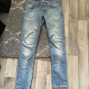 Nudie Jeans ljusblå straight jeans - Säljer ett par Nudie Jeans i ljusblå tvätt med klassiska orangea sömmar och snygga broderade detaljer på bakfickorna. Modellen har rak passform och normal midja. Materialet är mjukt jeans i bomull, perfekt för dig som gillar stilrena och bekväma jeans.Använde nästan aldrig dem pågrund av storlek dem blev för små 😂