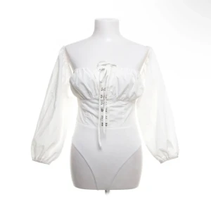 Vit korsett-topp PrettyLittleThing - Supersnygg vit korsett-topp från PrettyLittleThing med puffiga långärmar och snörning framtill. Toppen har en croppad passform och är axelbandslös med elastisk kant upptill. Pris kan diskuteras 