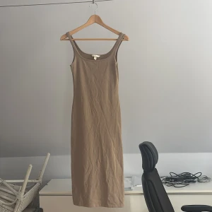 Beige långklänning från H&M - Säljer en stilren beige långklänning från H&M i storlek XS. Klänningen är ärmlös med smala axelband och har en rak, kroppsnära passform. Materialet är mjuk bomull som känns skönt mot huden. Perfekt för dig som gillar minimalistisk och clean stil.