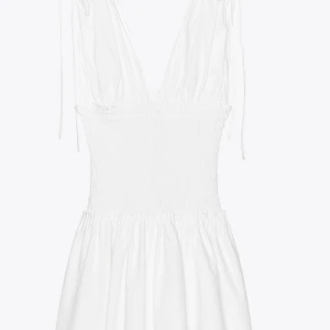 Vit kort klänning med smock och v-ringning - Supersöt vit klänning med smockad midja och djup v-ringning. Axelbanden är tunna och kan knytas för en personlig passform. Kjolen är lätt utställd och ger en flowy känsla. Perfekt för varma dagar och sommarhäng.💓💓