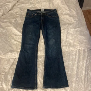 Mörkblå bootcut jeans från lager 157 - Snygga mörkblå jeans från lager 157 med klassisk bootcut-passform och kontrastsömmar. Jeansen har fem fickor, bälteshällor och en läderpatch med logga bak i midjan. Materialet är robust denim som ger en cool och tidlös vibe.