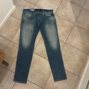 Replay Anbass hyperflex blå jeans, storlek 33/32 - Snygga Replay Anbass jeans i klassisk blå tvätt med ljusa slitningar på lår och bak. Normal passform och raka ben. Jeansen är tillverkade i stretchigt denim för extra komfort. Använda ett fåtal gånger.