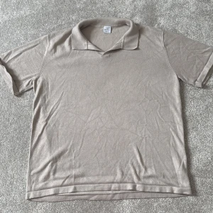 Beige pikétröja från Lindex - Snygg beige pikétröja från Lindex med klassisk krage och korta ärmar. Tröjan är gjord i mjuk bomull och har en stilren, enkel design utan mönster eller detaljer. Perfekt för dig som gillar en clean och chill look.