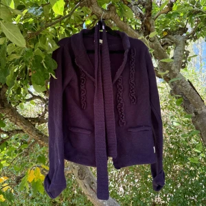 Lila stickad kofta från Odd Molly - Säljer en lila stickad kofta från Odd Molly med snygga virkade detaljer framtill och ett långt knytband. Koftan har två fickor och långa ärmar, perfekt för dig som gillar unika plagg med coola detaljer. Passar dig som vill ha en mysig och stilren look. Storlek 3 som enligt deras storleksguide motsvarar en storlek M/L.  Den är mer använd. Ytludd och noppror finns. Materialet är ull och nylon. 