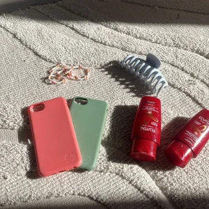 Litet kit med olika saker mobilskal är till iPhone 8 och shammpot o balsamet är oandvänt  - Ingen bok syns på bilderna, endast mobilskal, hårklämma, pärlhalsband och hårvårdsprodukter visas. Ingen information om någon boktitel, författare eller innehåll kan utläsas från bilderna.