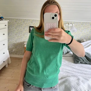 Grön stickad topp från Saint - Snygg grön stickad topp från Saint med korta ärmar och rund hals. Modellen har lätt puff vid axlarna och bred ribbad kant nedtill. Perfekt till jeans eller kjol för en fräsch look.