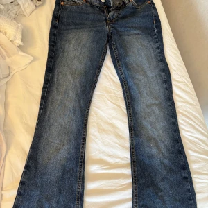 Blå bootcut jeans från Junkyard - Snygga blå jeans från Junkyard med bootcut passform och coola kontrastsömmar på bakfickorna. Klassisk femficksmodell med bälteshällor och läderpatch bak i midjan. Perfekta för dig som gillar en avslappnad men trendig look.