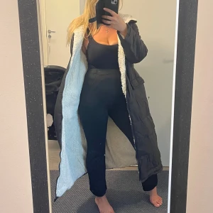 Lång svart pufferjacka med fuskpälsfoder - Säljer en lång svart pufferjacka med mysigt vitt fuskpälsfoder på insidan. Jackan har dragkedja framtill, stora fickor och en skön huva. Perfekt för kalla dagar när du vill hålla dig varm och ändå se snygg ut.Helt ny