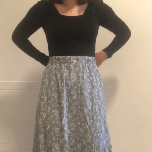 Blommig blå långkjol med fickor - Supersöt blå långkjol med vitt blommigt mönster och praktiska fickor. Kjolen har en hög midja med resår och är lätt och flowy, perfekt för att ge en chill och feminin vibe. Passar dig som gillar romantiska detaljer och vill ha något som sticker ut. Storlek L