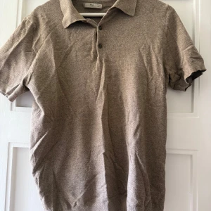 Beige pikétröja från Mango - Säljer en stilren beige/ brun pikétröja från Mango med klassisk krage och tre knappar framtill. Väldigt luftig i materialet använd typ 3 gånger 