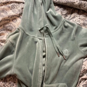 Grön velour hoodie från Juicy Couture - Säljer en mjuk och chill grön hoodie från Juicy Couture i velour med dragkedja och snörning vid huvan. Klassisk JC-logga broderad på bröstet och fickor framtill. Perfekt för att maxa cozy-viben.