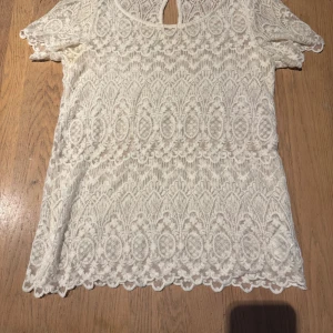 Vit spetsblus med kort ärm - Superfin vit blus i spets med korta ärmar och vackert broderat mönster. Blusen har rund halsringning och en liten knapp i nacken. 