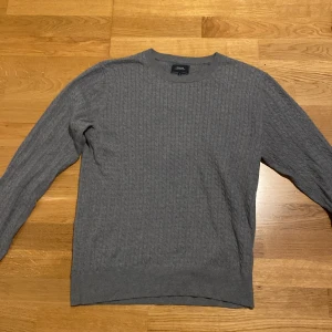 Grå kabelstickad tröja Boomerang - Säljer en grå kabelstickad tröja från Boomerang i storlek M. Tröjan har rund hals, ribbade muddar och ett klassiskt mönster som ger en chill och stilren vibe. Perfekt för lager-på-lager under hösten och vintern.