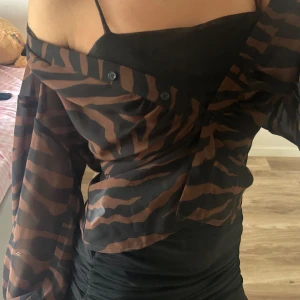 Brun och svart zebramönstrad skjorta från GinaTricot - Snygg transparent skjorta med zebramönster i brunt och svart. Skjortan har lång ärm, knappar framtill och en loose passform. Perfekt att styla över ett linne eller klänning för en cool look. Materialet känns lätt och luftigt.