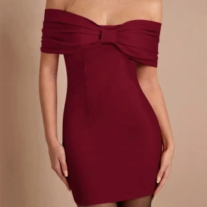 Vinröd offshoulder kortklänning med rosett - Supersnygg vinröd kortklänning med offshoulder och stor rosett framtill. Klänningen har en tight passform och är perfekt för dig som vill sticka ut. Materialet känns mjukt och följsamt, och den axelbandslösa designen ger en elegant vibe.