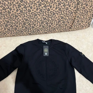 Svart Stone Island sweatshirt - Svart sweatshirt från Stone Island med stort broderat logomärke på bröstet och klassisk patch på vänster arm. Perfekt för dig som gillar streetwear och snygga detaljer. Storleken passar som M 