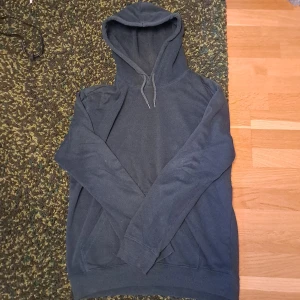 Mörkgrön hoodie från H&M, relaxed fit - En enkel och stilren mörkgrå hoodie från H&M i relaxed fit. Tröjan har huva med snörning, långa ärmar och en klassisk känguruficka framtill. Perfekt för chill dagar eller när du vill ha en avslappnad look.