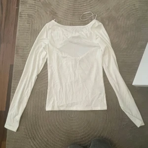 Vit långärmad topp med rosettdetalj - Säljer en vit långärmad topp från H&M med snygg rosettdetalj Toppen har en figurnära passform och är tillverkad i mjuk bomullsmix. Perfekt för dig som gillar trendiga detaljer och stilren look.