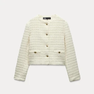 Vit kavajjacka från Zara - Snygg vit kavajjacka från Zara med strukturerat tyg och guldfärgade knappar. Jackan är croppad, har rund hals och två fickor framtill. Använd fåtal gånger