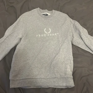 Grå sweatshirt från Fred Perry - Säljer en stilren grå sweatshirt från Fred Perry i storlek S. Tröjan har klassisk rund hals, lång ärm och vit logotyp med lagerkrans tryckt på bröstet. 
