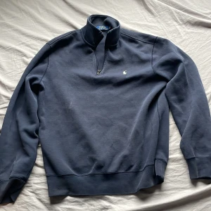 Marinblå half zip tröja Polo Ralph Lauren - Nytt pris 2100Snygg marinblå långärmad tröja från Polo Ralph Lauren med half zip och ståkrage. Tröjan har det klassiska broderade Polo-logot på bröstet och är gjord i mjuk bomull. Perfekt för dig som gillar stilren och sportig look. Liten flöck som enkelt försvinner i tvätten