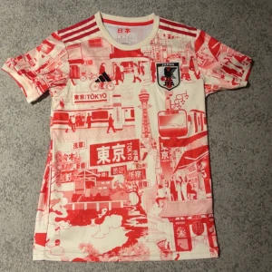 Japan Tokyo special edition fotbollströja Storlek M - Unik Japan fotbollströja från Adidas med Tokyo-inspirerat rött och vitt stadsmotiv över hela tröjan. Klassiska tre ränder på axlarna, JFA-emblem på bröstet och japanska flaggan i nacken. Tillverkad i lätt och ventilerande polyester. Perfekt för dig som vill sticka ut på läktaren.