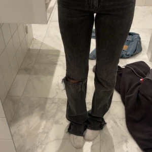 Grå svarta jeans med hål  - Säljer ett par svarta jeans i storlek 32. Jeansen har ett hål på knät och fransiga benslut. Modellen är rak med normal passform och något högmidjade. Perfekta i längd 