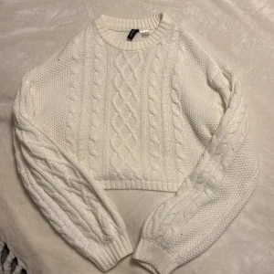 Vit stickad croppad tröja H&M - Superfin vit stickad tröja från HM Divided i croppad modell. Tröjan har ett klassiskt flätmönster, rund halsringning och långa ärmar med ribbade muddar. Perfekt för lager-på-lager och ger en mysig vibe till din outfit💝🛍️är i bra skick☺️