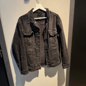 Svart jeansjacka från ZARA, storlek M - Snygg svart jeansjacka från ZARA i klassisk modell med knappar framtill och två bröstfickor med lock. Jackan har raka ärmar och coola sömdetaljer som ger en stilren vibe. Perfekt att slänga över en hoodie eller t-shirt för en avslappnad look.